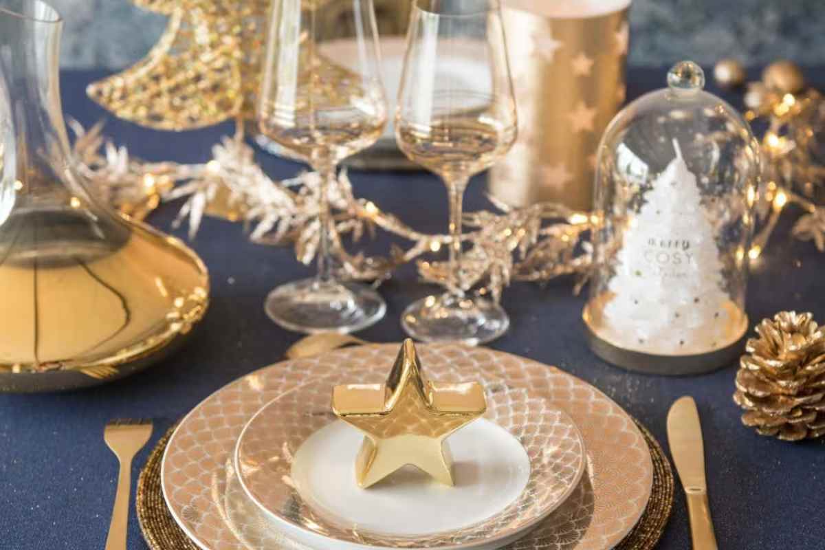 una tavola apparecchiata in modo elegante con piatti e, decorazioni dorate e candele natalizie Maisons du Monde