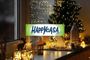 angolo di casa addobbato con luci e piccolo alberello di natale e in primo piano il logo di happy casa