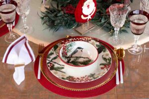 particolare della mise en place di natale con bicchieri della nonna vintage, tovaglia in fiandra e piatti moderni decorati con uccelli