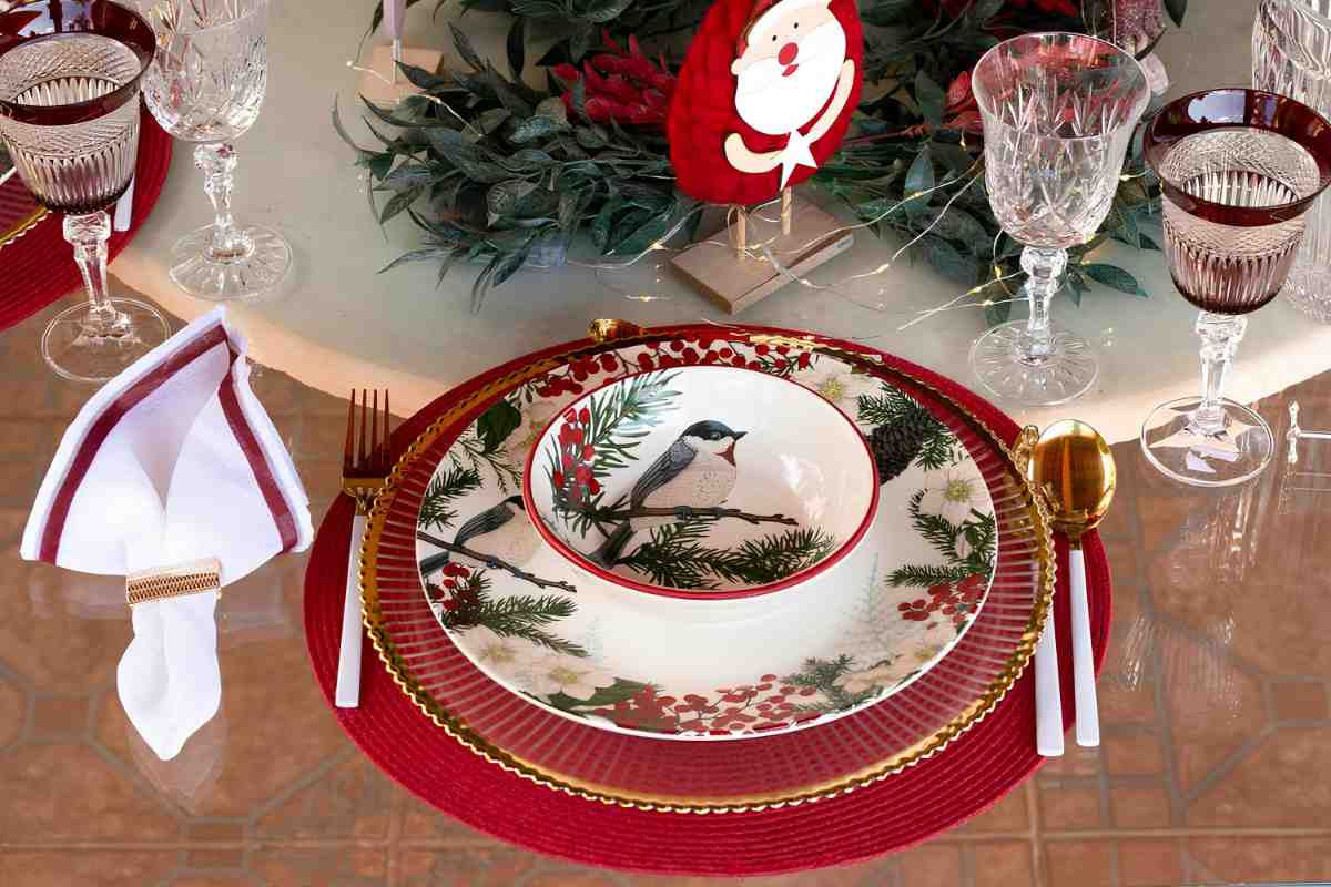 particolare della mise en place di natale con bicchieri della nonna vintage, tovaglia in fiandra e piatti moderni decorati con uccelli