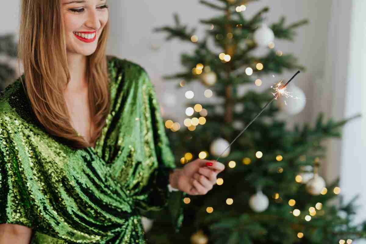 donna in abito elegante con scintille in mano e albero di Natale sullo sfondo